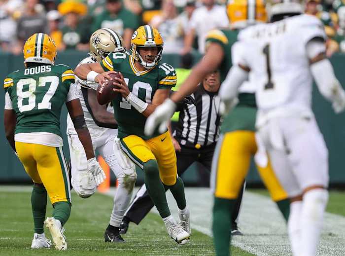 Jordan Love runs with the ball in two hands as a Saints player chases him